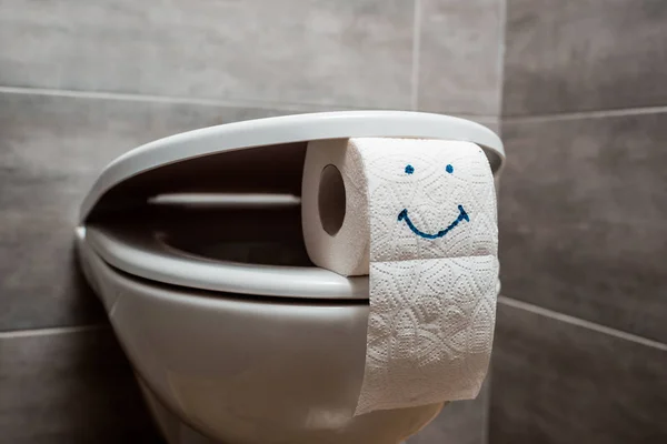 Vue rapprochée de la cuvette de toilette propre en céramique et du papier toilette avec visage souriant dans les toilettes modernes — Photo de stock