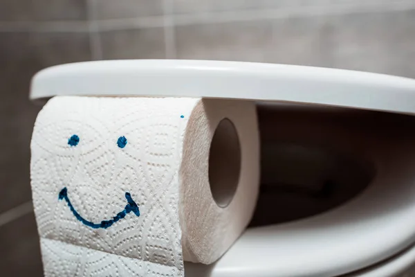 Vue rapprochée de la cuvette de toilette propre en céramique et du papier toilette avec visage souriant dans les toilettes modernes — Photo de stock