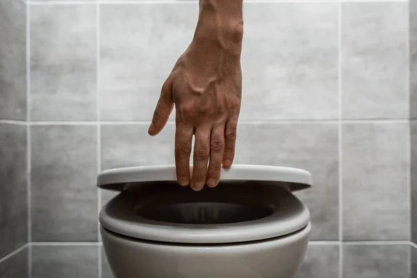 Vista recortada del hombre sosteniendo tapa del inodoro en el baño moderno con baldosas grises - foto de stock