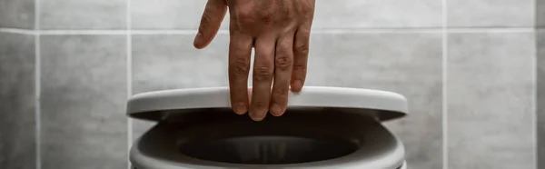 Cropped view of man holding toilet lid in modern restroom with grey tile, panoramic shot — Stock Photo