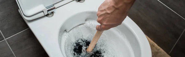 Cropped view of plumber using plunger in toilet bowl during flushing in modern restroom with grey tile, panoramic shot — Stock Photo