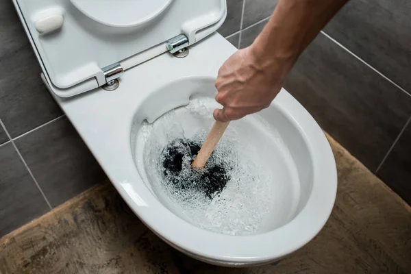 Vista ritagliata dell'idraulico usando lo stantuffo nella tazza del water durante lo scarico nel bagno moderno con piastrelle grigie — Foto stock