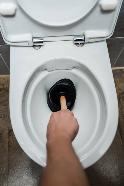 Vista cortada de encanador usando êmbolo em vaso sanitário no banheiro moderno com azulejo cinza — Fotografia de Stock