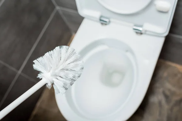 Selective focus of ceramic toilet bowl and clean toilet brush in modern restroom with grey tile — Stock Photo