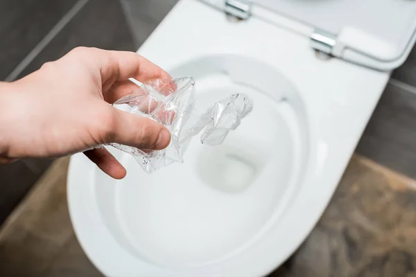 Vista ritagliata di uomo gettando bottiglia di plastica accartocciata nella tazza del water in bagno moderno con piastrelle grigie — Foto stock