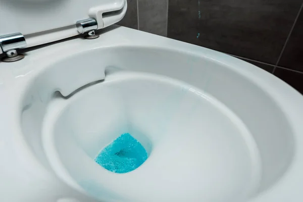 Vue rapprochée du détergent liquide bleu dans un bol de toilette propre en céramique dans les toilettes modernes avec tuile grise — Photo de stock