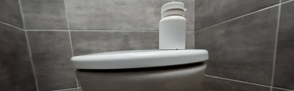 Récipient avec pilules sur un bol de toilette en céramique propre dans les toilettes modernes avec tuile grise, vue panoramique — Photo de stock