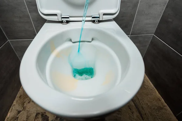 Detergente líquido azul vertiendo en el inodoro limpio de cerámica en el baño moderno con baldosas grises - foto de stock