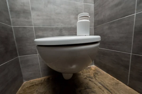 Контейнер з таблетками на керамічному чистому унітазі в сучасному туалеті з сірою плиткою — стокове фото
