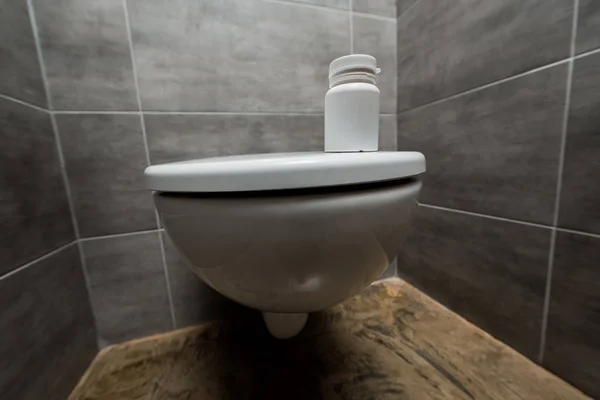 Container with pills on ceramic clean toilet bowl in modern restroom with grey tile — Stock Photo