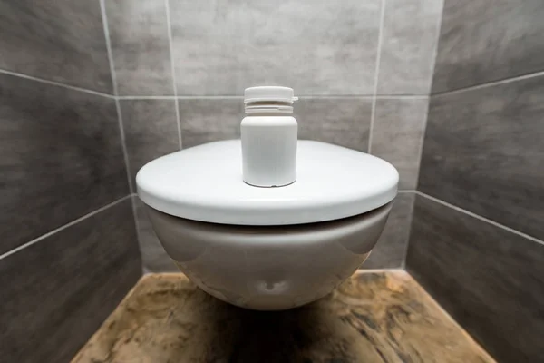 Контейнер з таблетками на керамічному чистому унітазі в сучасному туалеті з сірою плиткою — стокове фото