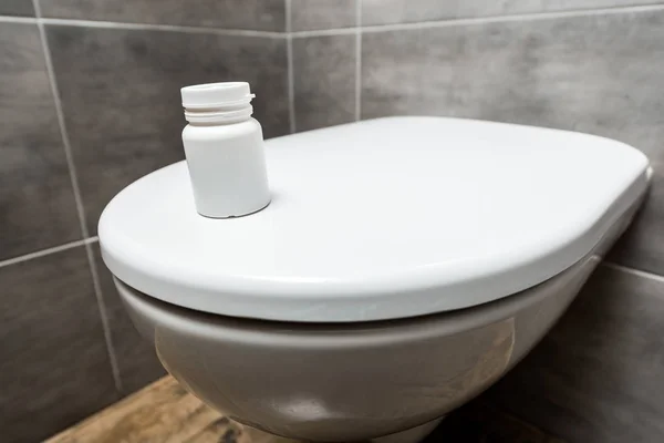 Récipient avec pilules sur bol de toilette propre en céramique dans les toilettes modernes avec tuile grise — Photo de stock