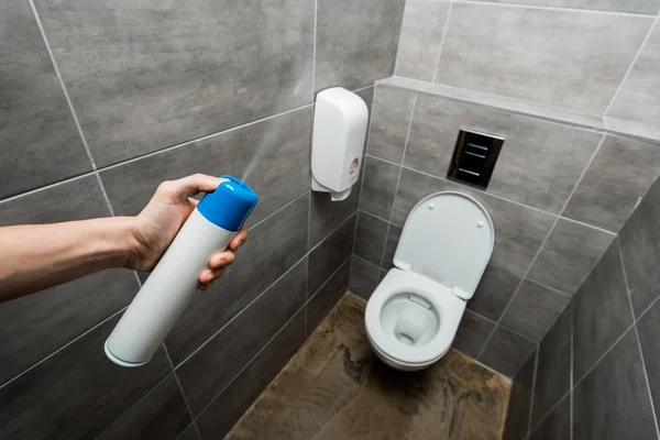 Cropped view of man spraying air freshener in modern restroom with grey tile — Stock Photo