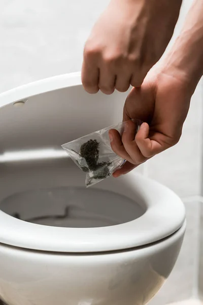 Visão cortada do homem jogando fora botões de maconha em vaso sanitário — Fotografia de Stock