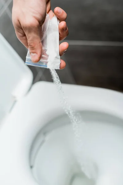 Cropped view of man pouring out cocaine in toilet bowl in modern restroom with grey tile — Stock Photo