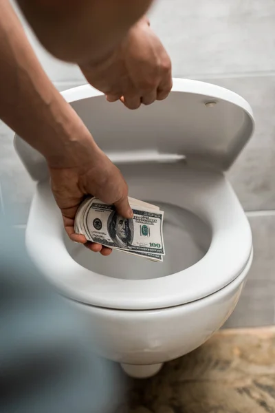 Vista cortada de homem jogando notas de dólar em vaso sanitário — Fotografia de Stock