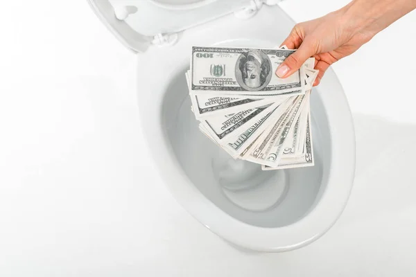 Cropped view of woman holding dollars near ceramic clean toilet bowl isolated on white — Stock Photo