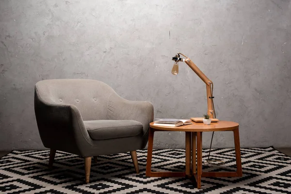 Интерьер гостиной с удобным серым современным креслом рядом с деревянным столом и лампой на ковре — стоковое фото