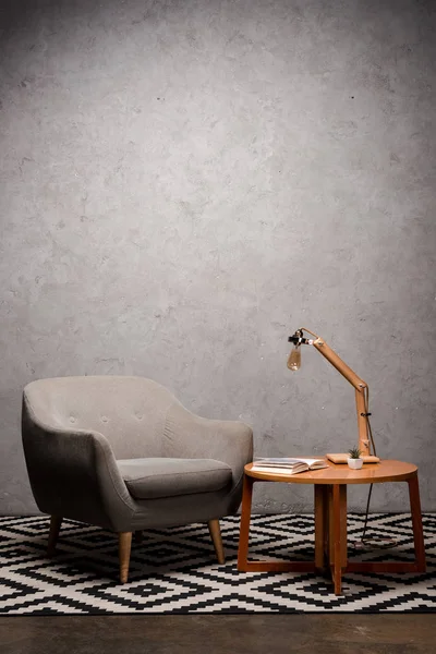Интерьер гостиной с удобным серым современным креслом рядом с деревянным столом и лампой на ковре — стоковое фото