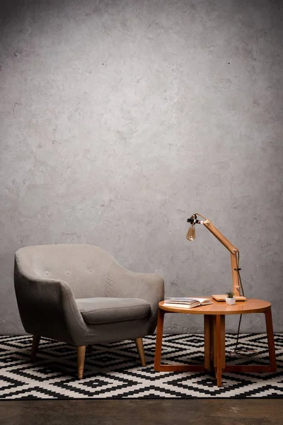 Interior de la sala de estar con cómodo sillón moderno gris cerca de mesa de madera y lámpara en la alfombra - foto de stock