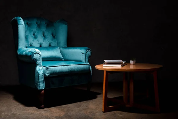 Élégant fauteuil en velours bleu près de la table en bois avec livre isolé sur noir — Photo de stock