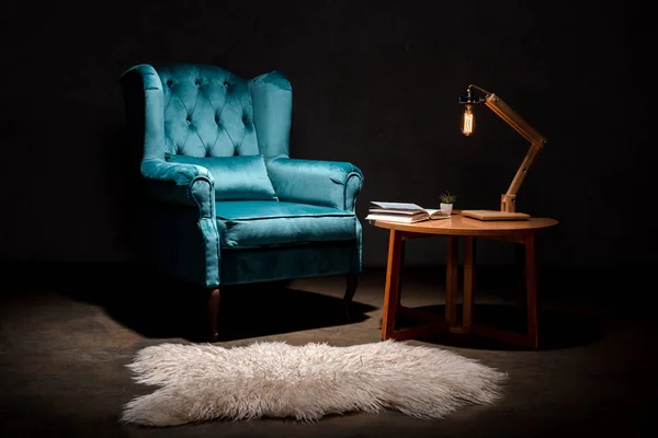 Elegant velour blue armchair with pillow near animal skin rug, wooden table and lamp isolated on black — Stock Photo