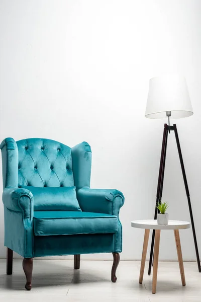 Élégant fauteuil bleu velours avec oreiller près de la table basse et lampadaire — Photo de stock