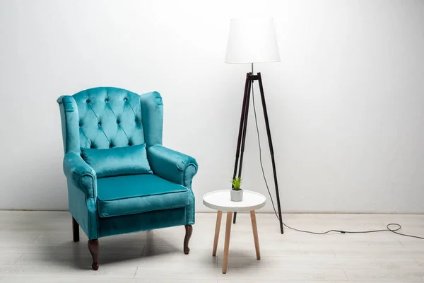 Élégant fauteuil bleu velours avec oreiller près de la table basse et lampadaire — Photo de stock