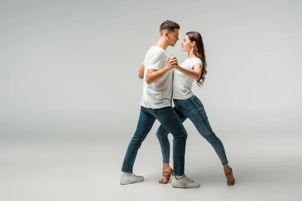 Bailarinos sorridentes em camisetas e jeans dançando bachata em fundo cinza — Fotografia de Stock