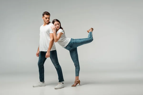 Танцоры в футболках и джинсах, танцующие бачату на сером фоне — стоковое фото