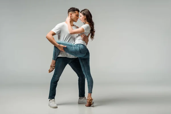 Danseurs en t-shirts et jeans dansant bachata sur fond gris — Photo de stock