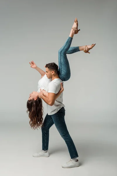 Vista lateral de dançarinos em camisetas e jeans bachata dançando em fundo cinza — Fotografia de Stock