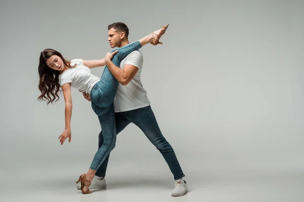 Bailarinas en camisetas y jeans bailando bachata sobre fondo gris - foto de stock