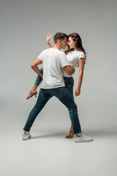 Dançarinos em camisetas e jeans bachata dançando em fundo cinza — Fotografia de Stock