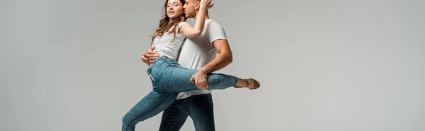 Panoramic shot of smiling dancers in t-shirts and jeans dancing bachata isolated on grey — Stock Photo