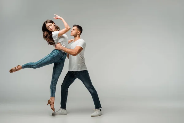 Tänzer in T-Shirts und Jeans tanzen Bachata auf grauem Hintergrund — Stockfoto