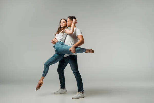 Bailarinos sorridentes em camisetas e jeans dançando bachata em fundo cinza — Fotografia de Stock