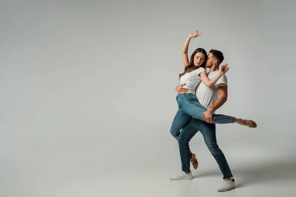 Dancers in t-shirts and jeans dancing bachata on grey background — Stock Photo