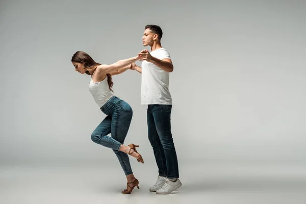 Вид збоку танцюристів у джинсах, танцююча баната на сірому фоні — стокове фото