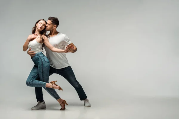 Tänzer in Jeans tanzen Bachata auf grauem Hintergrund — Stockfoto