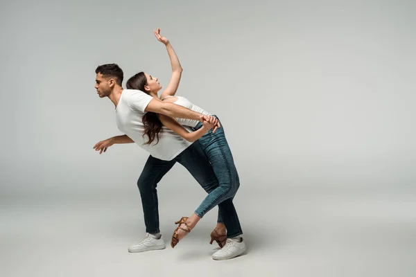 Vue latérale des danseurs en jeans denim dansant bachata sur fond gris — Photo de stock