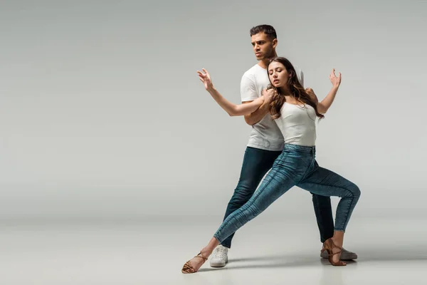 Танцюристи в джинсах танцюють баната на сірому фоні — стокове фото