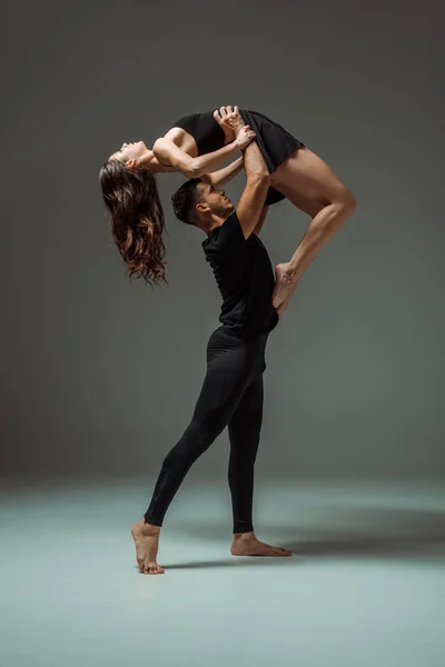 Side view of handsome and attractive dancers dancing contemporary on dark background — Stock Photo