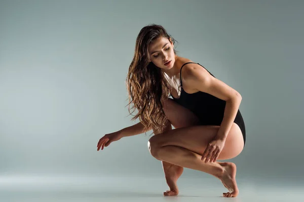 Atractiva bailarina de body negro bailando contemporáneo sobre fondo gris - foto de stock