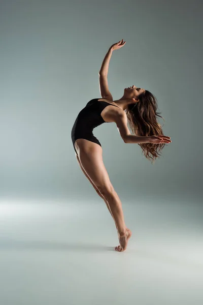 Vue latérale d'une danseuse séduisante en body noir dansant contemporaine sur fond gris — Photo de stock