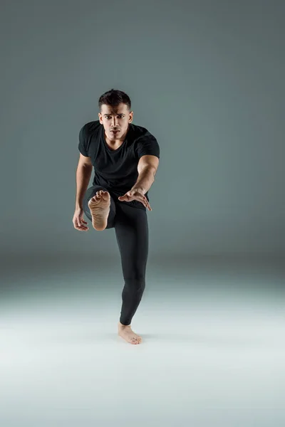 Hermosa bailarina de polainas negras y camiseta bailando contemporáneo sobre fondo oscuro - foto de stock