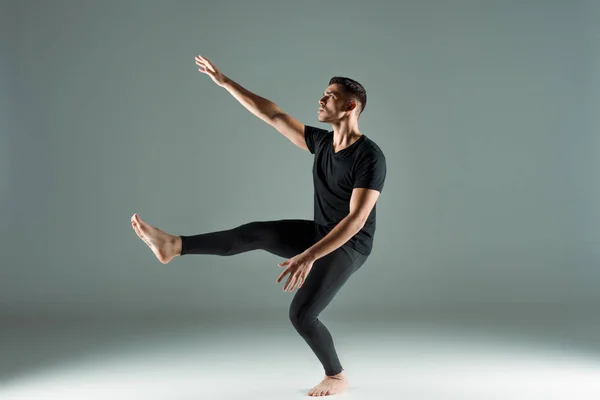Hübsche Tänzerin in schwarzen Leggings und T-Shirt, die zeitgenössisch auf dunklem Hintergrund tanzt — Stockfoto