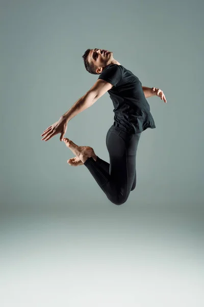 Hermosa bailarina de polainas negras y camiseta bailando contemporáneo sobre fondo oscuro - foto de stock