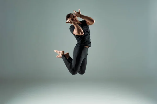 Hübsche Tänzerin mit geschlossenen Augen in schwarzen Leggings und T-Shirt, die zeitgenössisch auf dunklem Hintergrund tanzt — Stockfoto