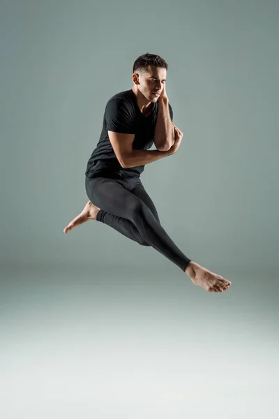 Hübsche Tänzerin mit geschlossenen Augen in schwarzen Leggings und T-Shirt, die zeitgenössisch auf dunklem Hintergrund tanzt — Stockfoto